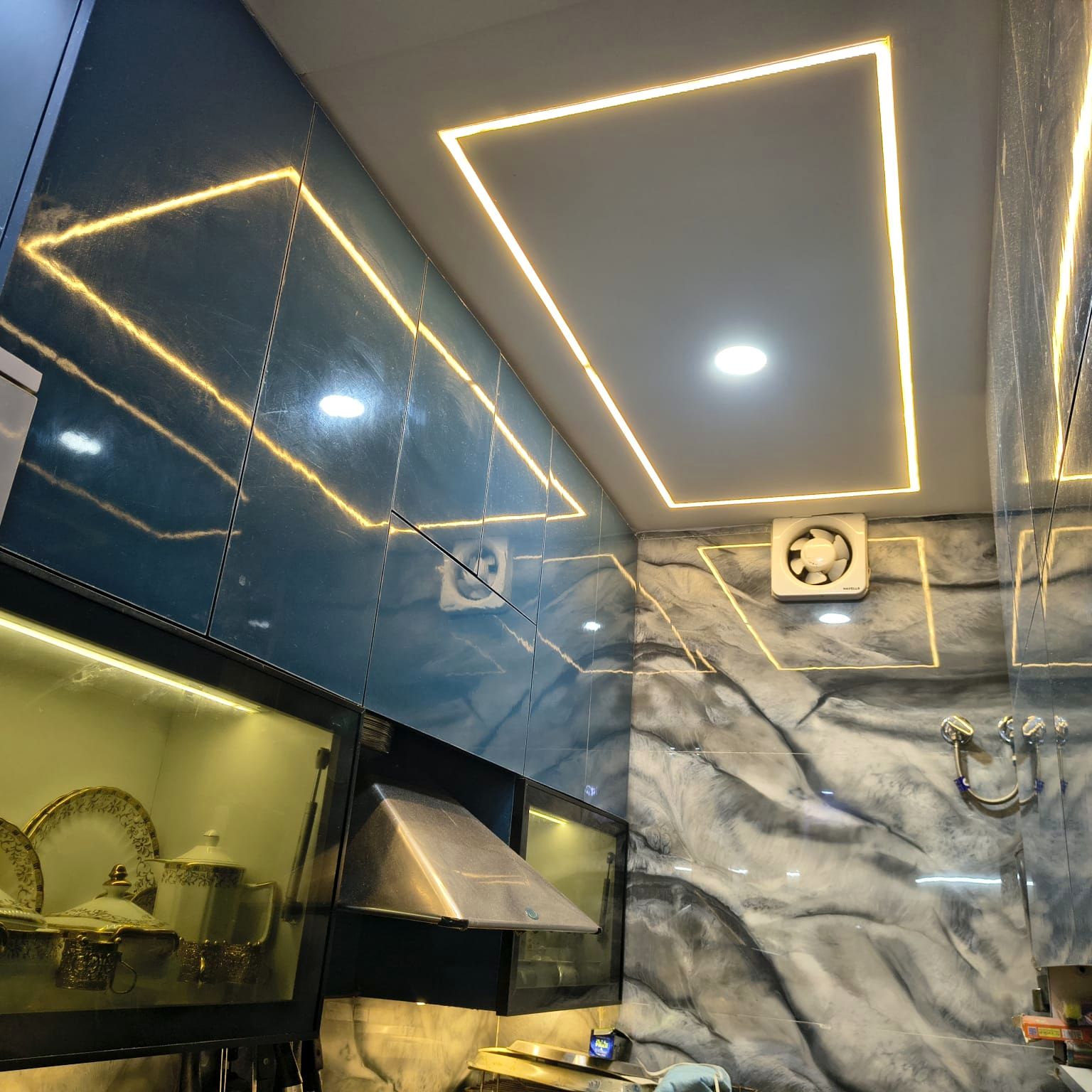 The same kitchen after work: glossy navy blue cabinets, a marble-pattern backsplash and a false ceiling with recessed profile lighting.