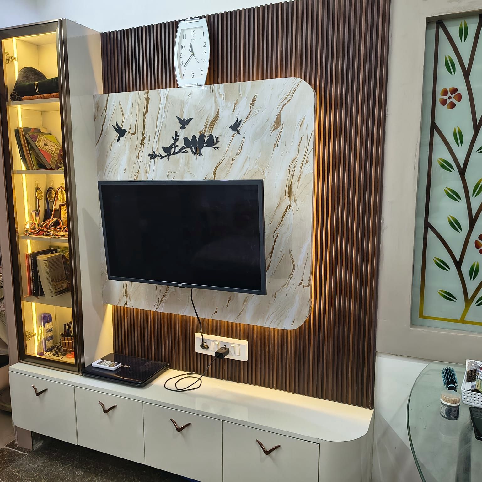 The same living room after work: a fluted walnut media wall with a stone-finish panel, backlit display shelving and a white handleless console.