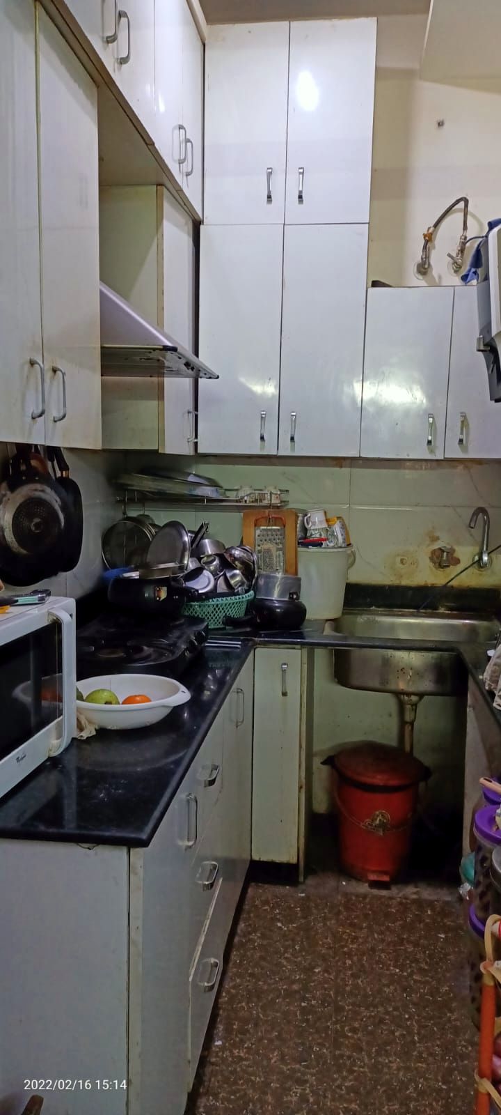 The kitchen before work: worn cream cabinets, an open shelf of utensils and a dated counter.